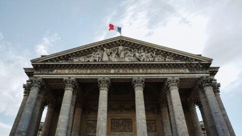 Paris Panthéon facade with six columns and sculpted pediment, French flag atop the roof.
