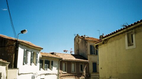 Row of pastel-colored houses with tiled roofs under a bright blue sky, a sunny urban street scene.