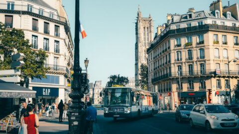 Busy Paris street with a city bus, pedestrians, and Haussmannian buildings; GAP storefront on the left.
