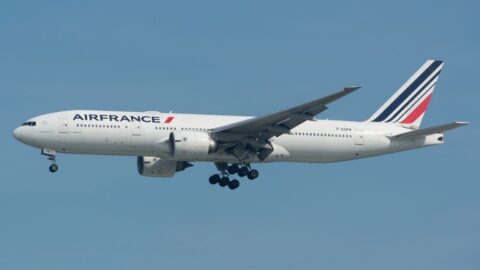 Air France passenger jet with landing gear extended flying against a clear blue sky, displaying the AIR FRANCE branding on the fuselage and a striped tail fin.