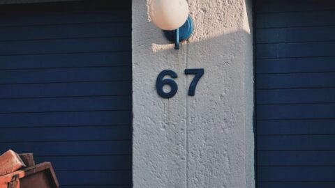 Exterior wall with the number 67 between blue shutters and a round light fixture above the column.