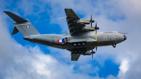 Military transport airplane in flight with four propellers and gray fuselage against a blue sky, French markings visible on the body.