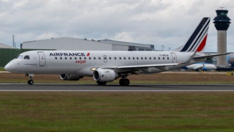 Air France jet taxiing on a runway with a control tower in the background.
